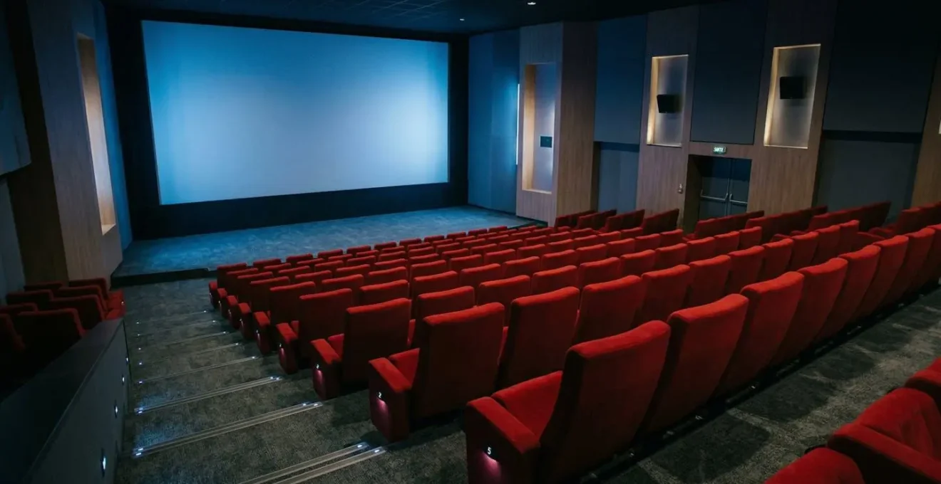 Grande salle de cinéma contemporaine avec écran illuminé et rangées de fauteuils rouges vus depuis le fond de la salle
